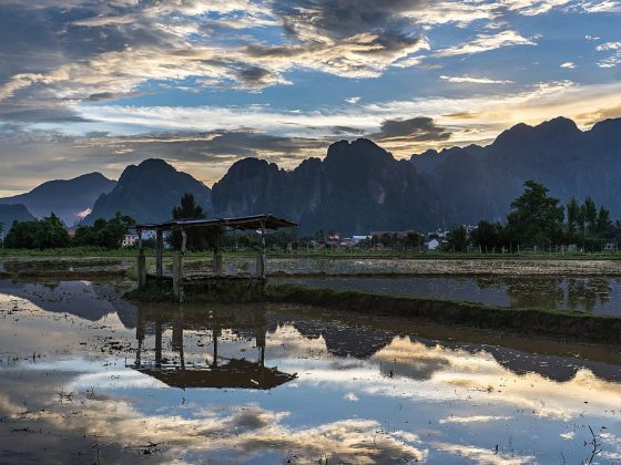 Water_reflection_of_a_wooden_hut_with_colorful_sky_and_karst_mountains_in_a_paddy_field_at_sunset_Vang_Vieng_Laos